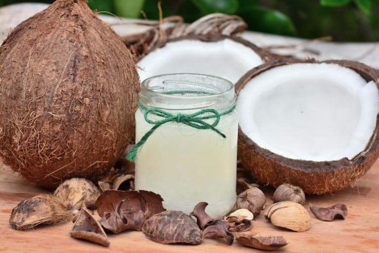 Raw coconuts surround a glass jar filled with coconut oil and tied with green twine